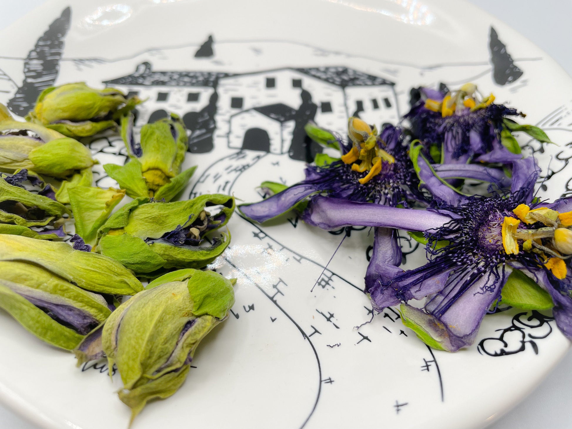 Dried passionflower blossoms (Passiflora incarnata) with purple petals, yellow stamens, and green sepals displayed on a decorative plate.